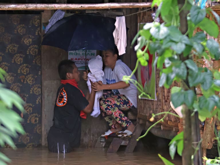 Pareja saca a su bebé ante la inundación que afecta a su hogar tras el paso de la tormenta tropical Jelawat en la isla de Mindanao en Filipinas.